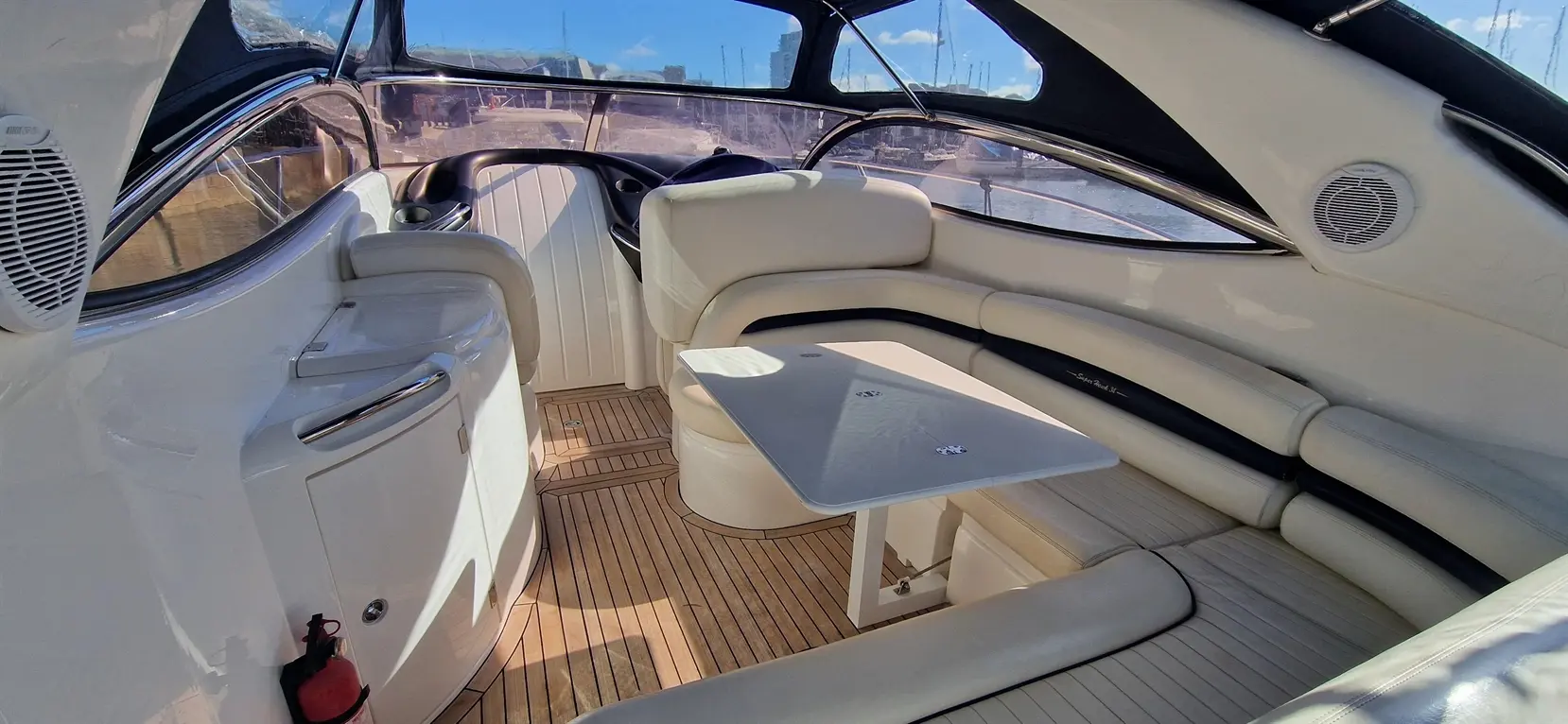 Spacious interior of a luxury boat featuring cream leather seating, a wooden floor, and a table by a large window.